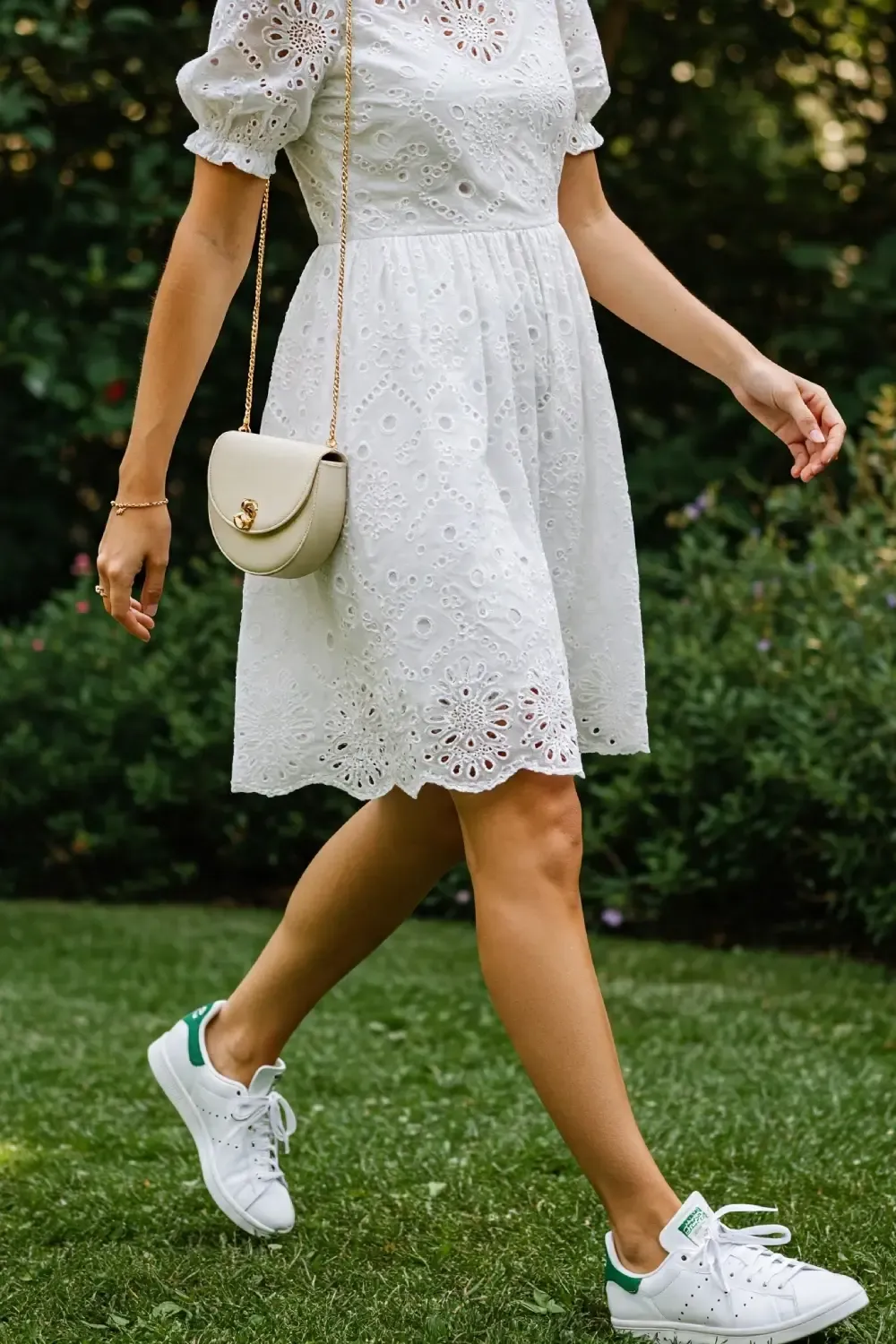 Woman walking in a white eyelet cotton sundress paired with Adidas Stan Smith sneakers and a small crossbody bag, creating an effortless summer look
