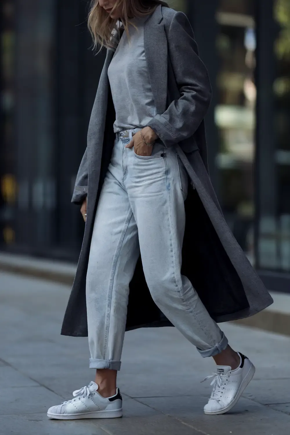 Street style outfit featuring light wash jeans, grey structured coat, simple t-shirt, and white Stan Smith sneakers for an elevated casual look