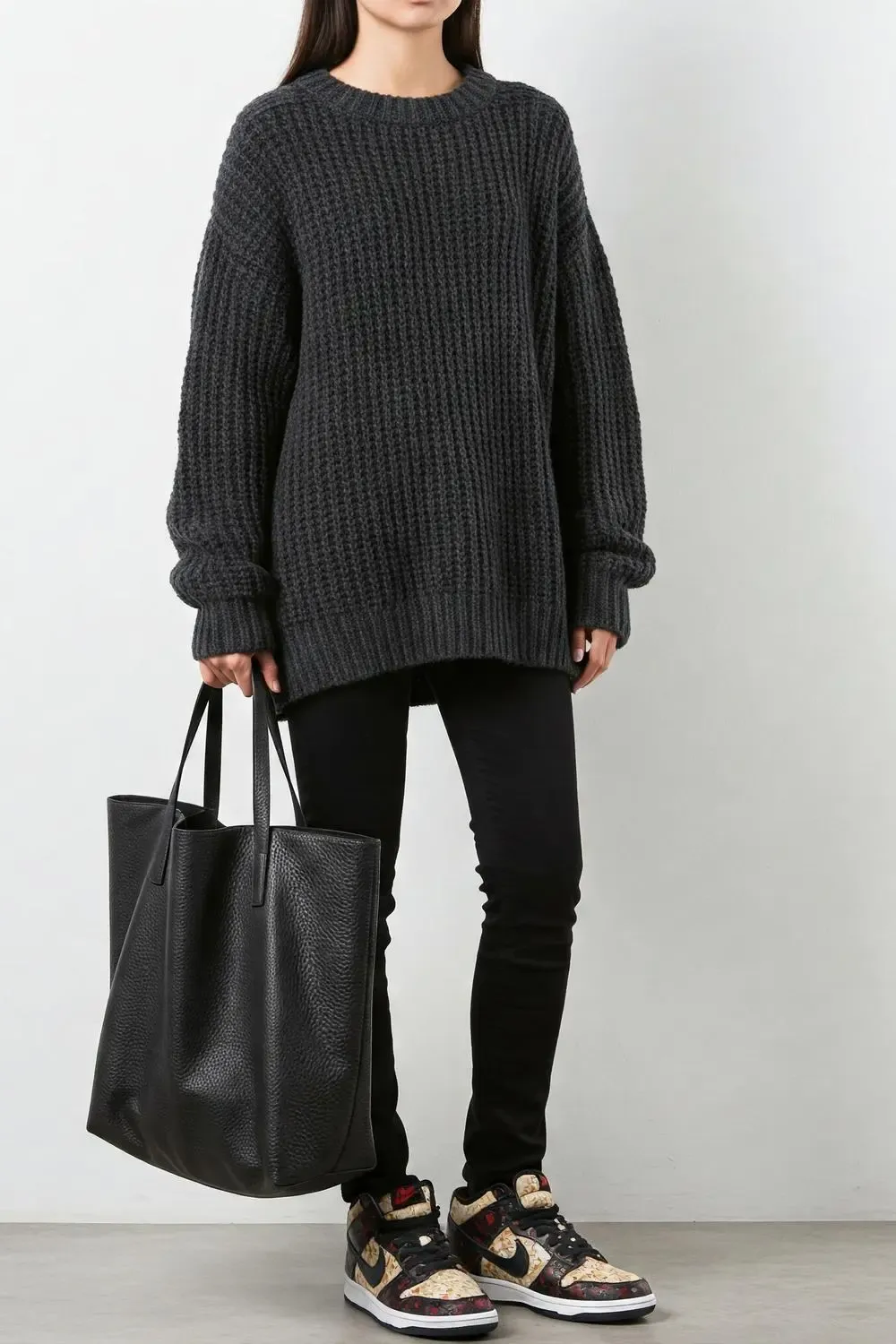 Woman balancing black skinny jeans and statement Nike Dunk Lows with an oversized chunky knit sweater for a chic, proportional look.