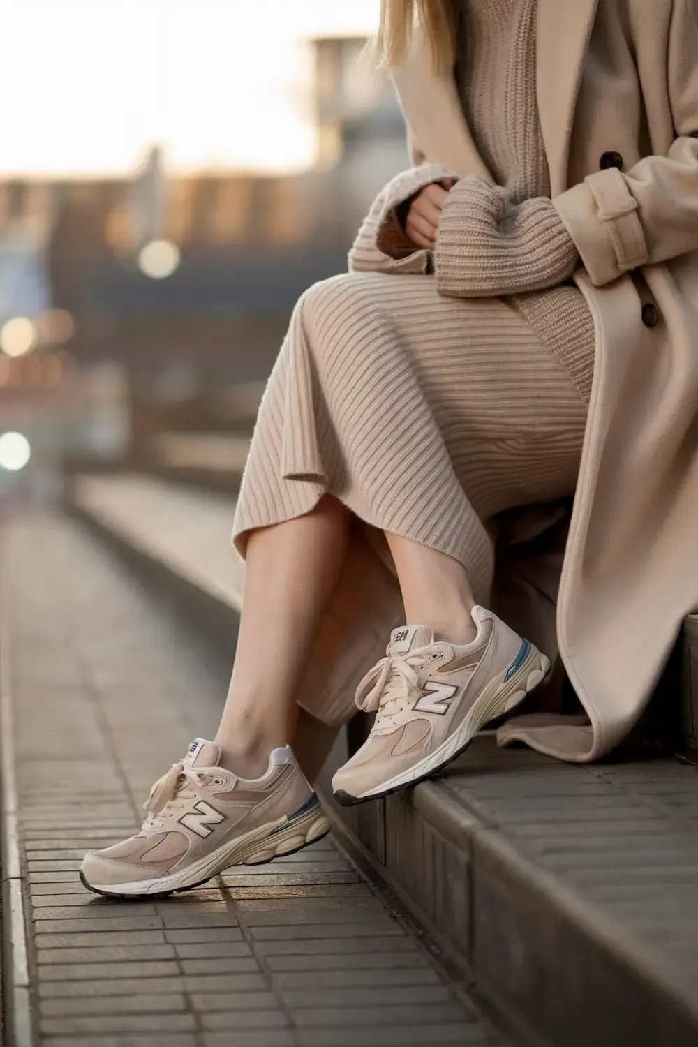Close-up detail shot of cream ribbed knit dress, beige coat, and beige New Balance sneakers, highlighting texture and color coordination in winter styling