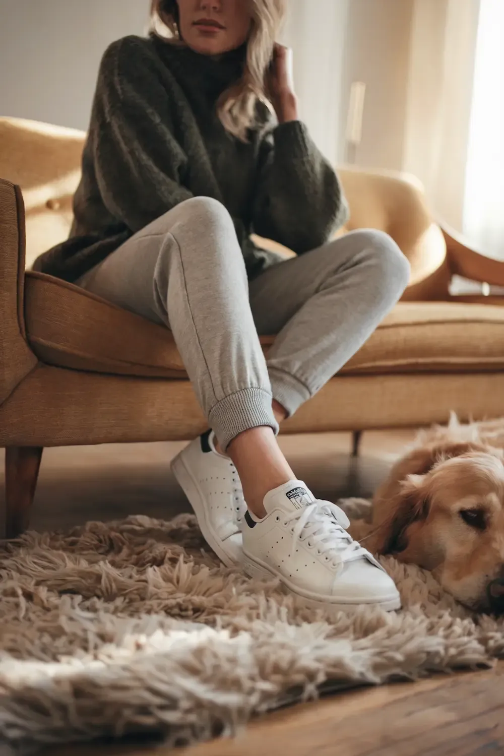 Dark grey oversized turtleneck sweater paired with light grey joggers and white sneakers with dog nearby - ultimate comfort work-from-home outfit for relaxed productivity on textured rug