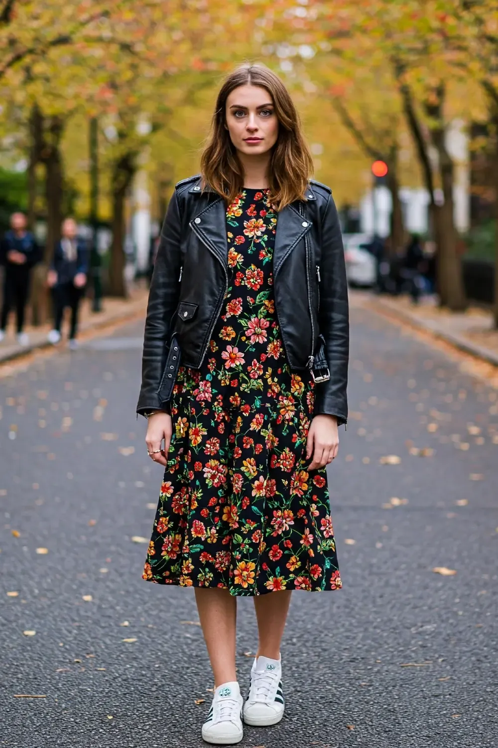 Woman wearing a floral midi dress with black leather jacket and white Adidas Samba OG sneakers on a tree-lined autumn street, demonstrating fall pattern mixing.
