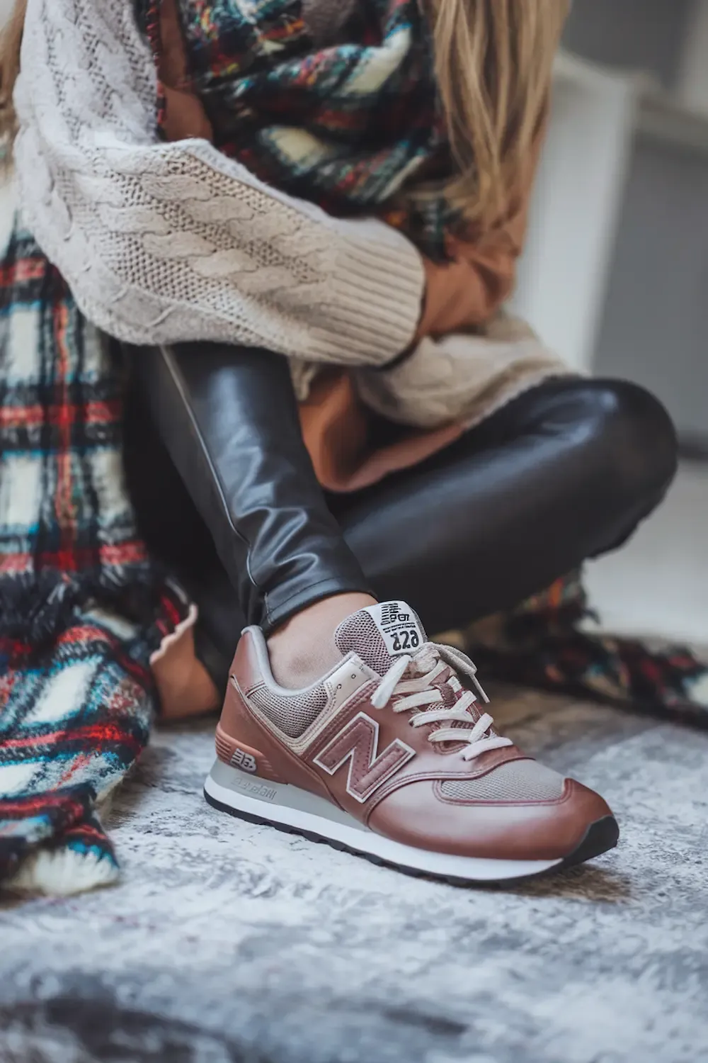 Close-up of rose gold New Balance sneaker styled with leather leggings, cable knit sweater and plaid scarf