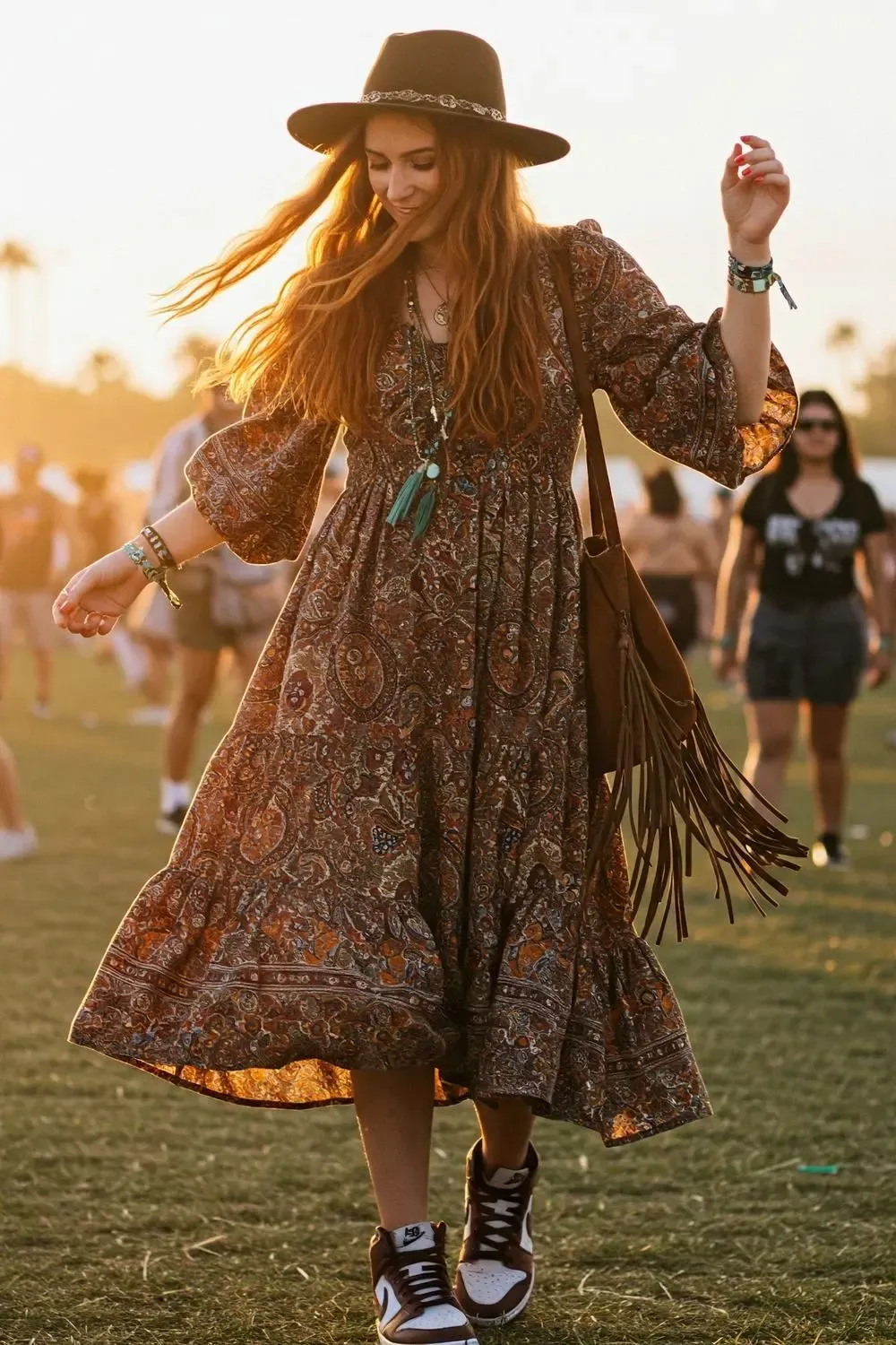 Woman in a flowy bohemian maxi dress and white Nike Dunk Lows, dancing at a festival during sunset.