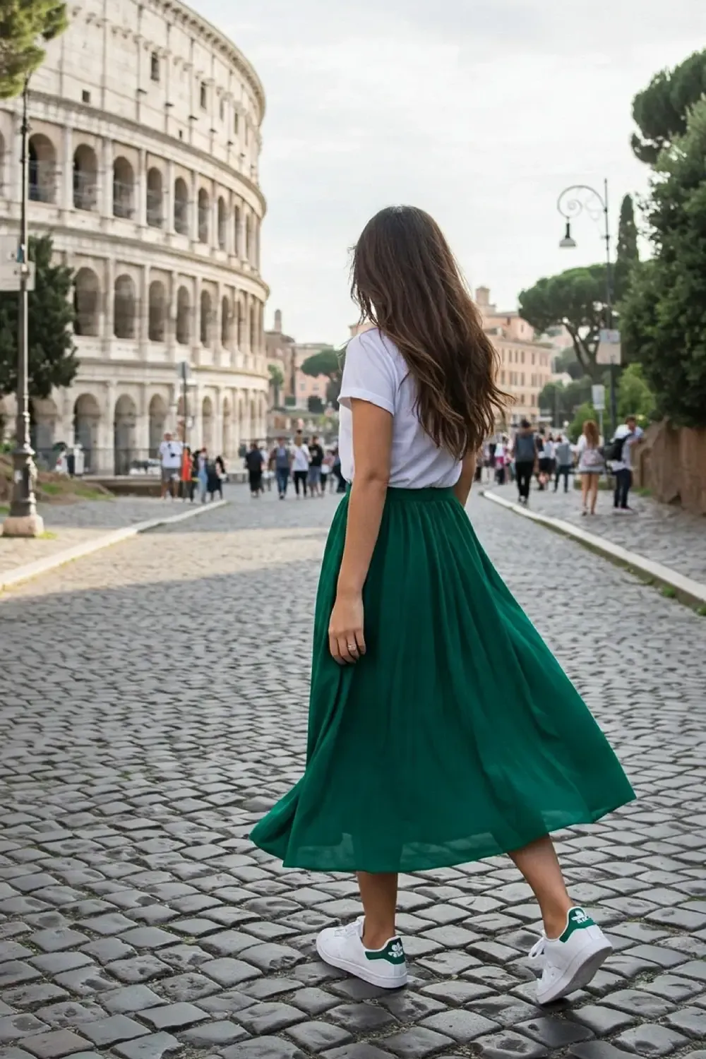 Woman in simple white t-shirt paired with flowing green midi skirt walking toward the Colosseum, showcasing how white sneakers complement dressy elements.