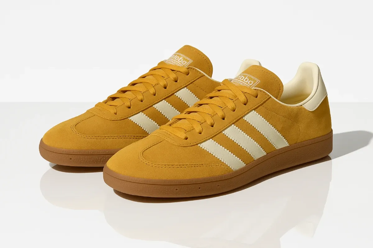 Adidas Handball Spezial in vibrant mustard yellow suede with off-white three stripes, gum rubber outsole, retro sports heritage design, reinforced toe cap, and classic T-toe construction inspired by vintage indoor court shoes.