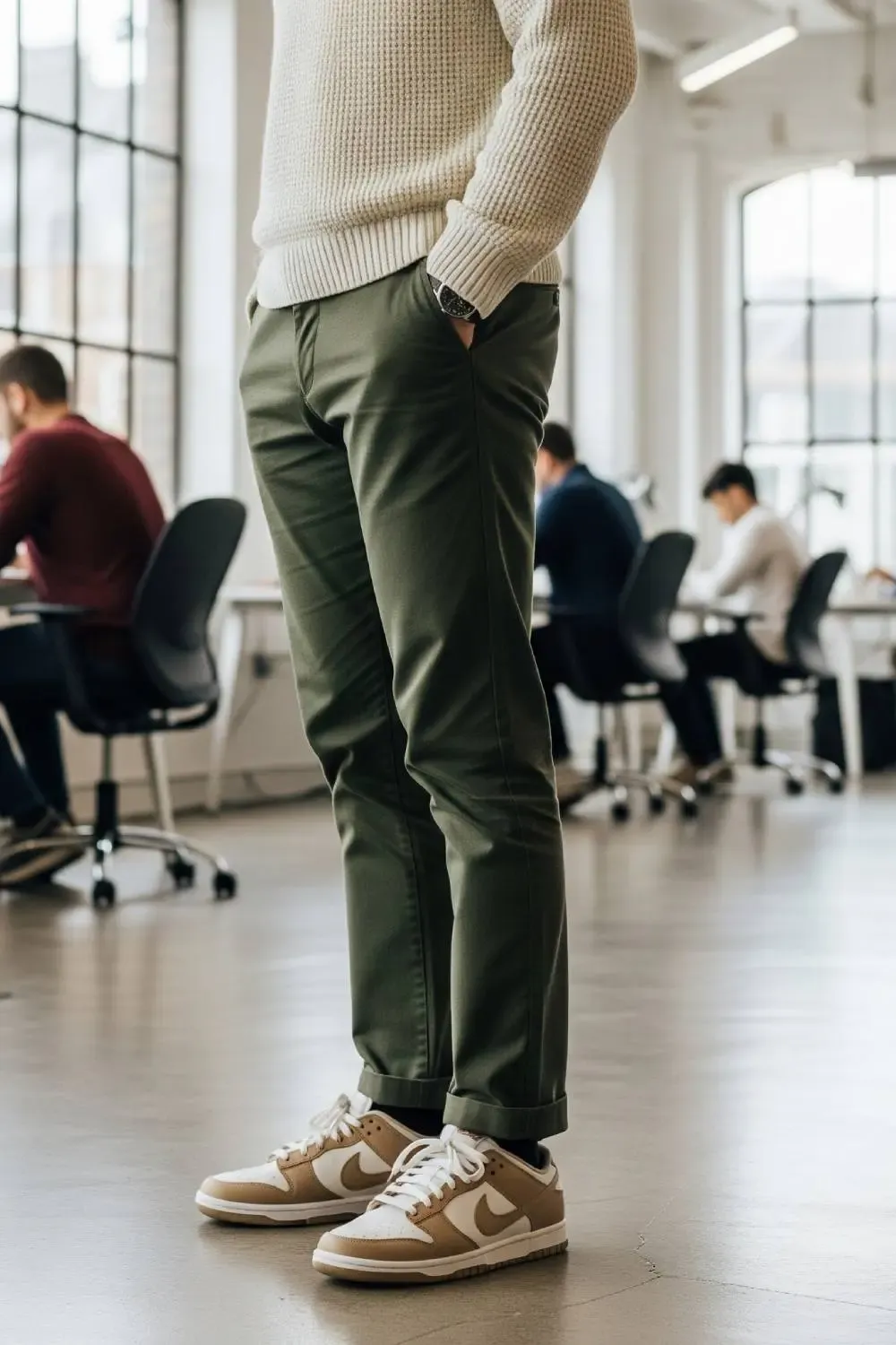 Man in a creative office setting wearing olive chinos, a cream sweater, and earth-toned Nike Dunk Lows