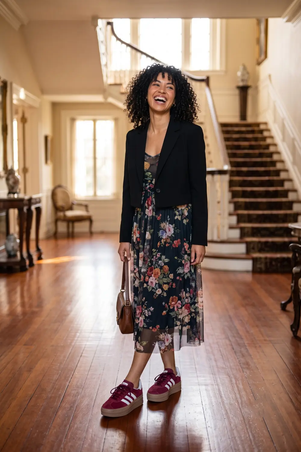 Lifestyle editorial photo of a 30-year-old woman with bouncy dark curls wearing a romantic floral mesh midi dress under a sharp cropped black blazer