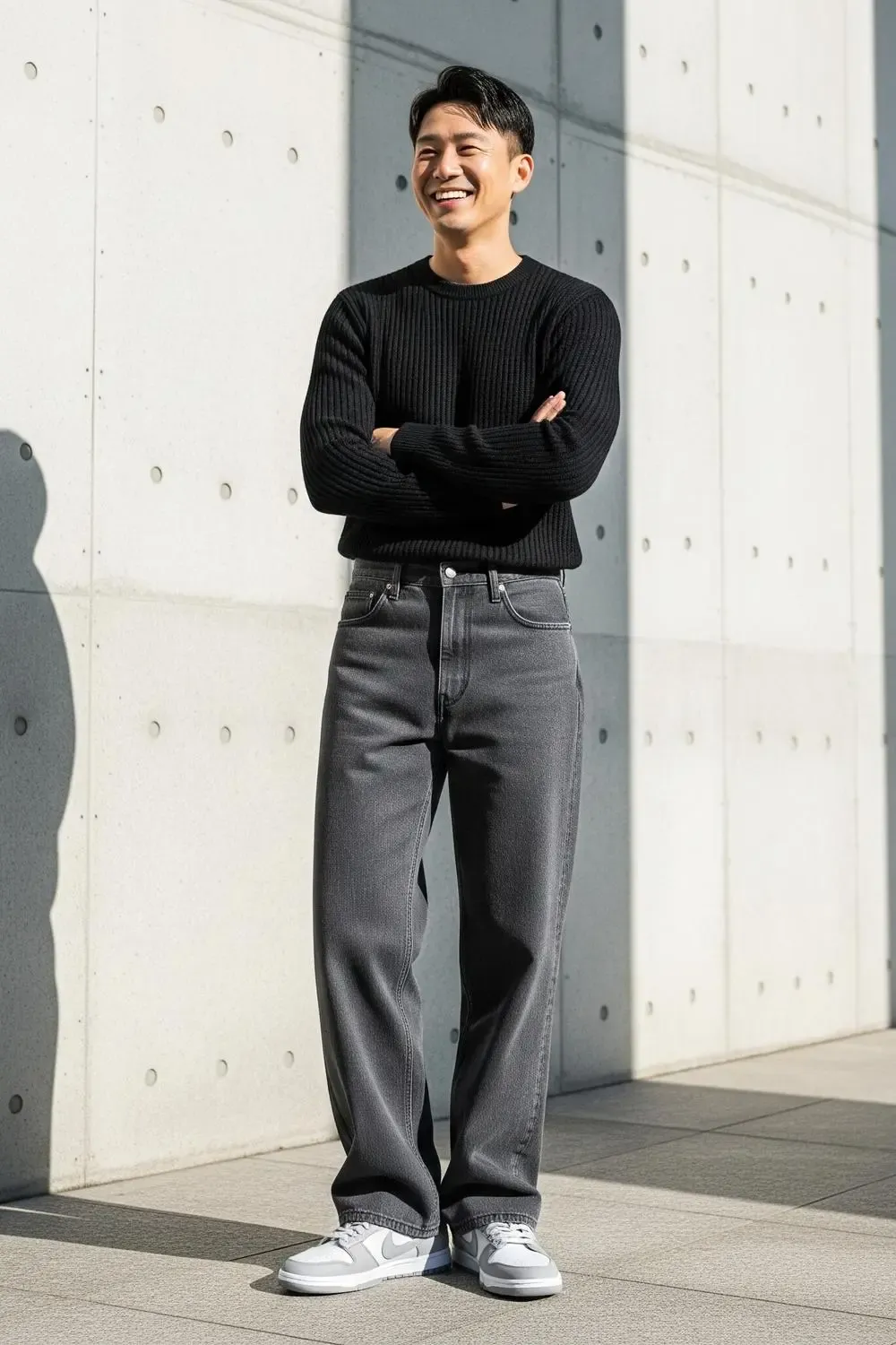 Man showcasing a monochrome minimalist outfit with Grey Fog Dunk Lows, grey wide-leg pants, and a black knit sweater.