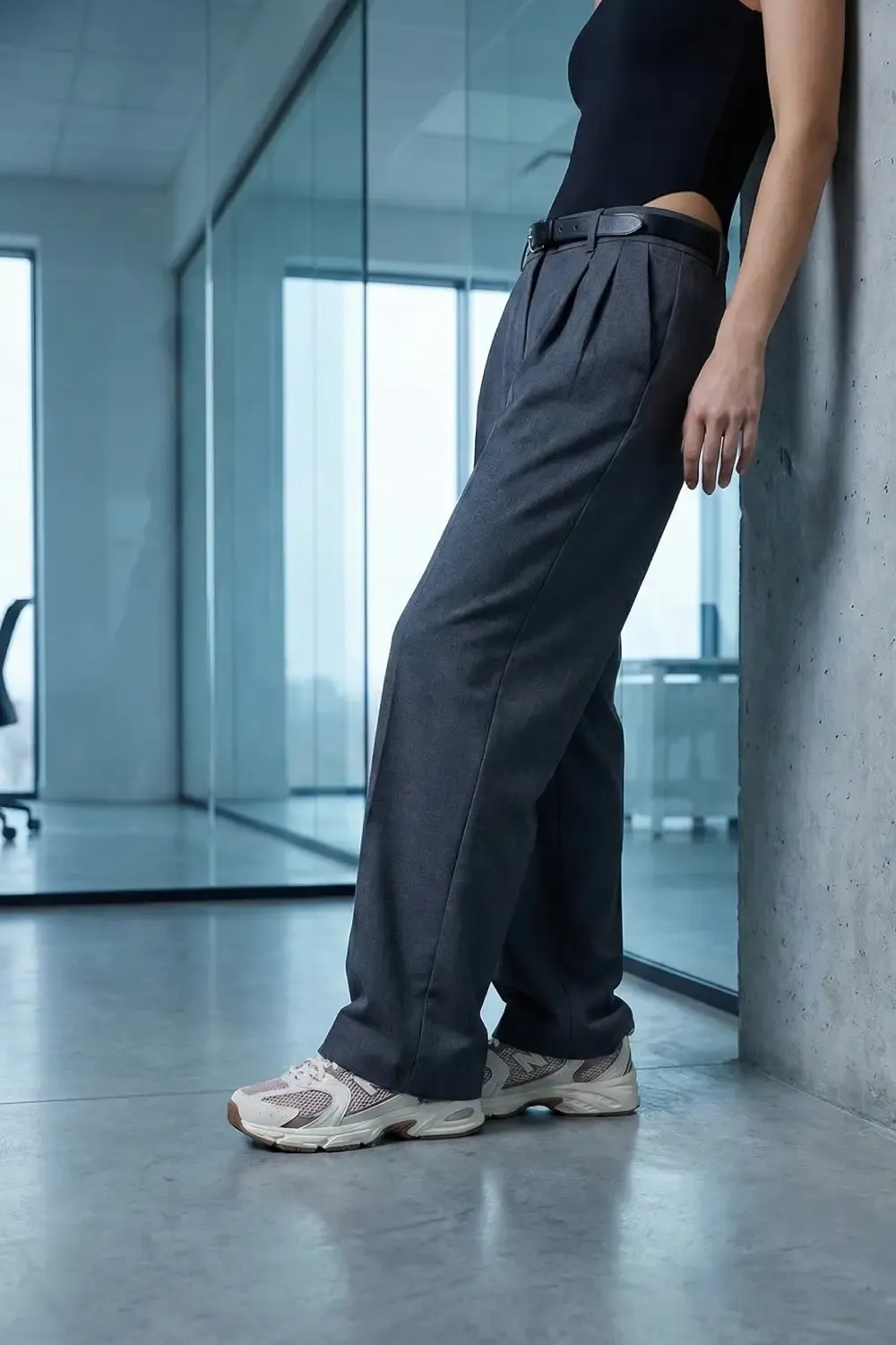 Woman wearing grey tailored trousers and New Balance 530 sneakers in a modern office setting.