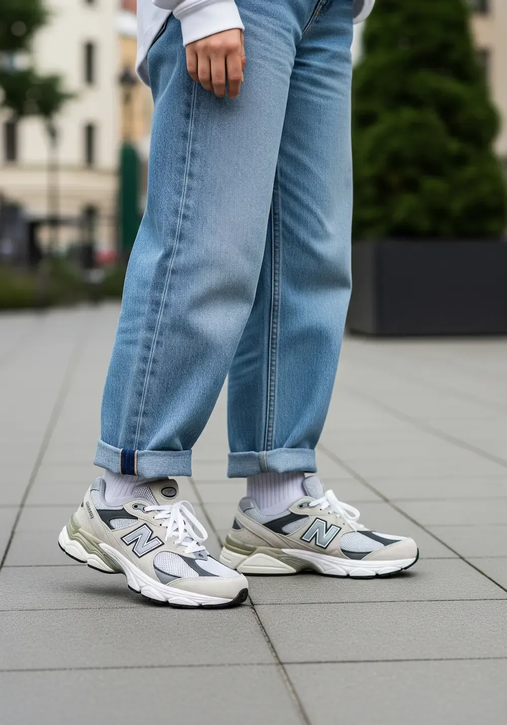 An on-foot, street-style shot of a person wearing New Balance 9060s with loose-fitting, light-wash baggy jeans, demonstrating how to style the chunky sneaker silhouette.