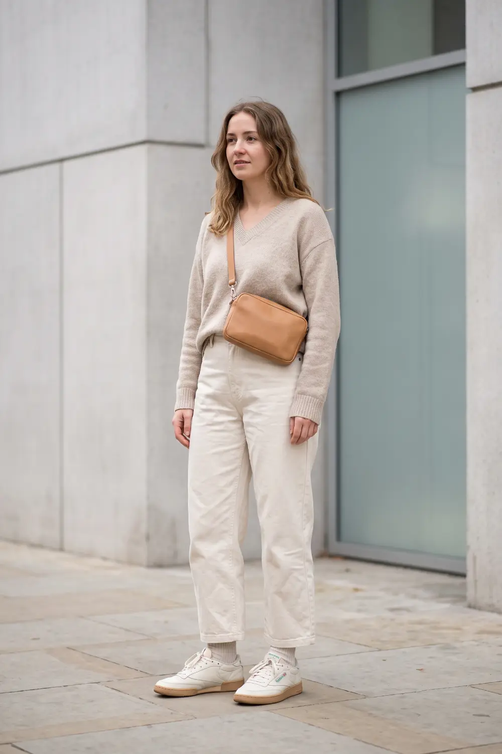 A beige normcore women's outfit consisting of cream-colored canvas pants, a beige sweater, and Reebok Club C 85 sneakers.